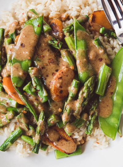 asparagus stir-fry with snow peas and carrots over a bed of rice and topped with almond butter sauce.