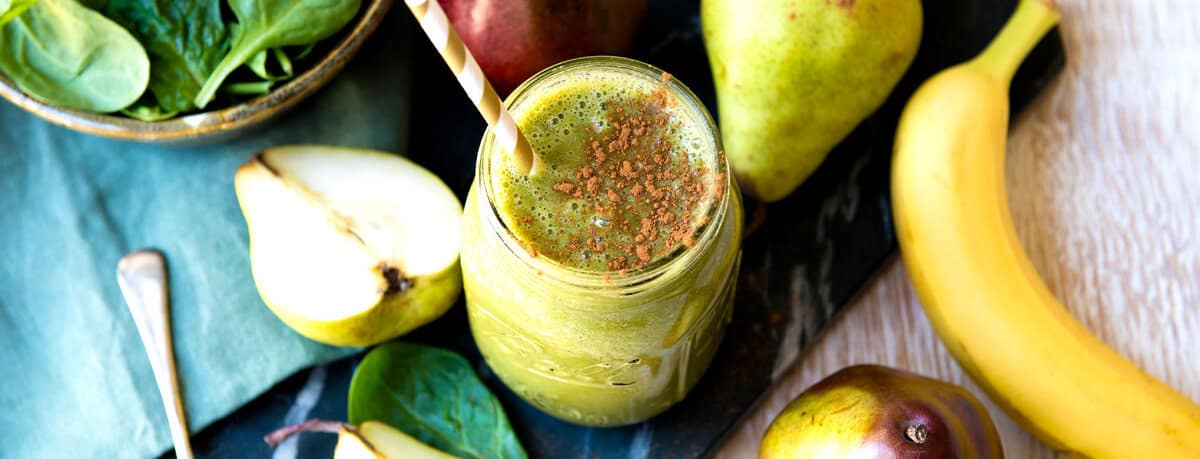 Healthy green smoothie in a glass with fresh pears and bananas around it.