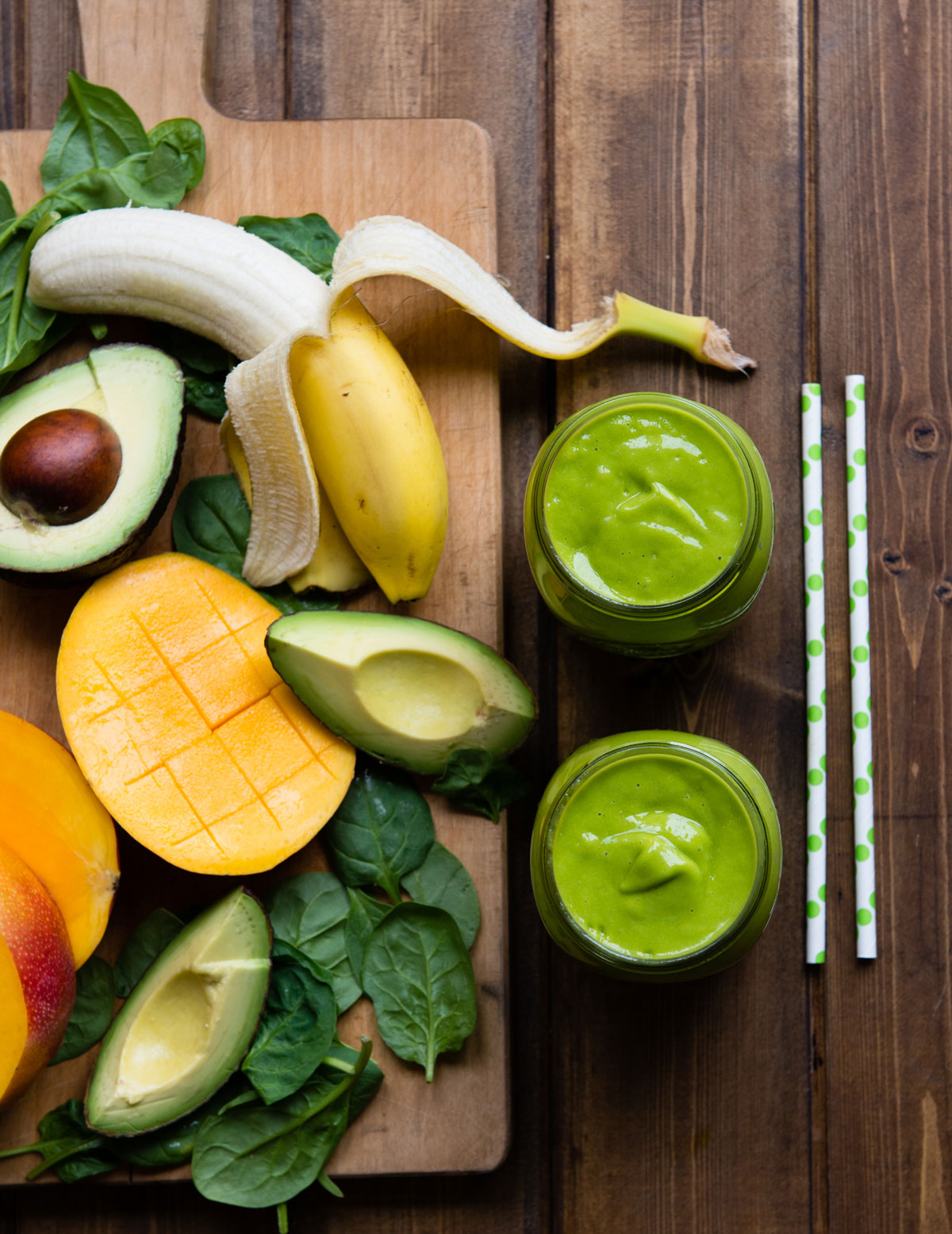 Cutting board with cut mango, avocado and spinach with glass of green smoothie.