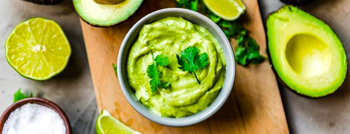 avocado crema in small bowl with fresh avocados, salt, and lime next to it