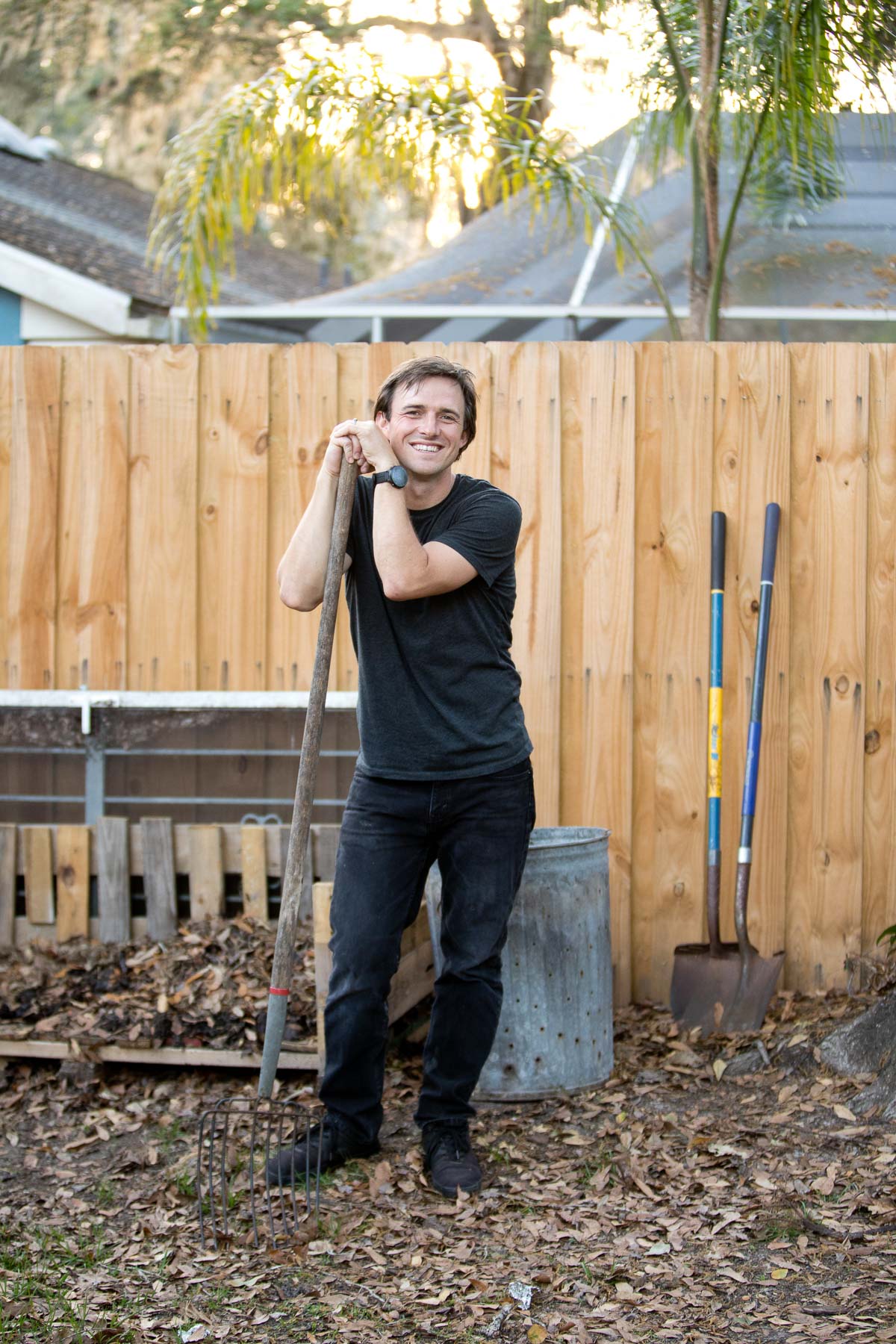Ryan next to his compost bin, leaning on his shovel.