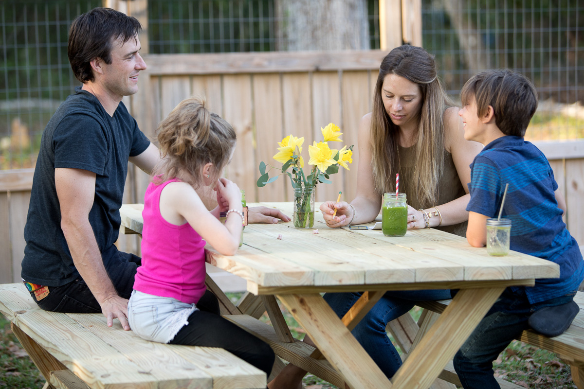 Jen and her family sitting around a picnic table enjoying green smoothies
