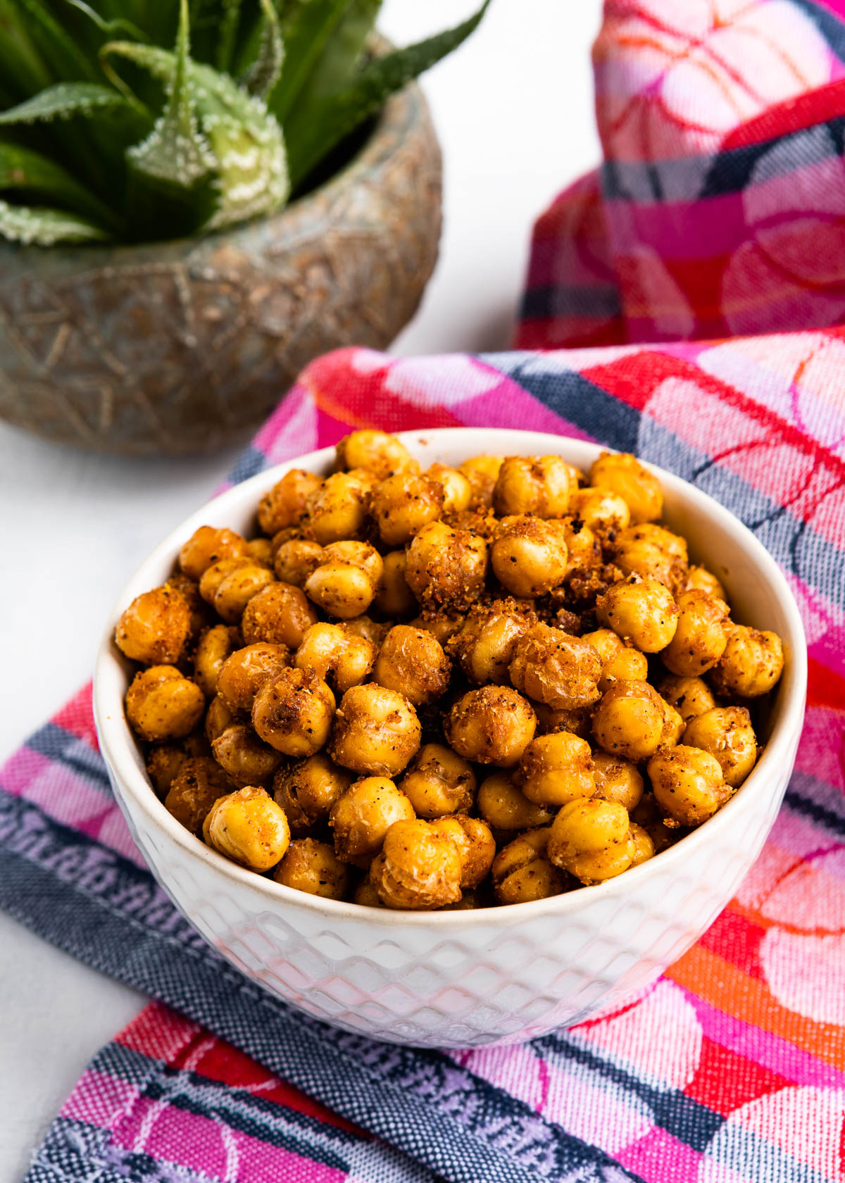 white bowl full of oven baked chickpeas full of seasoning, sitting on top of a colorful tea towel.