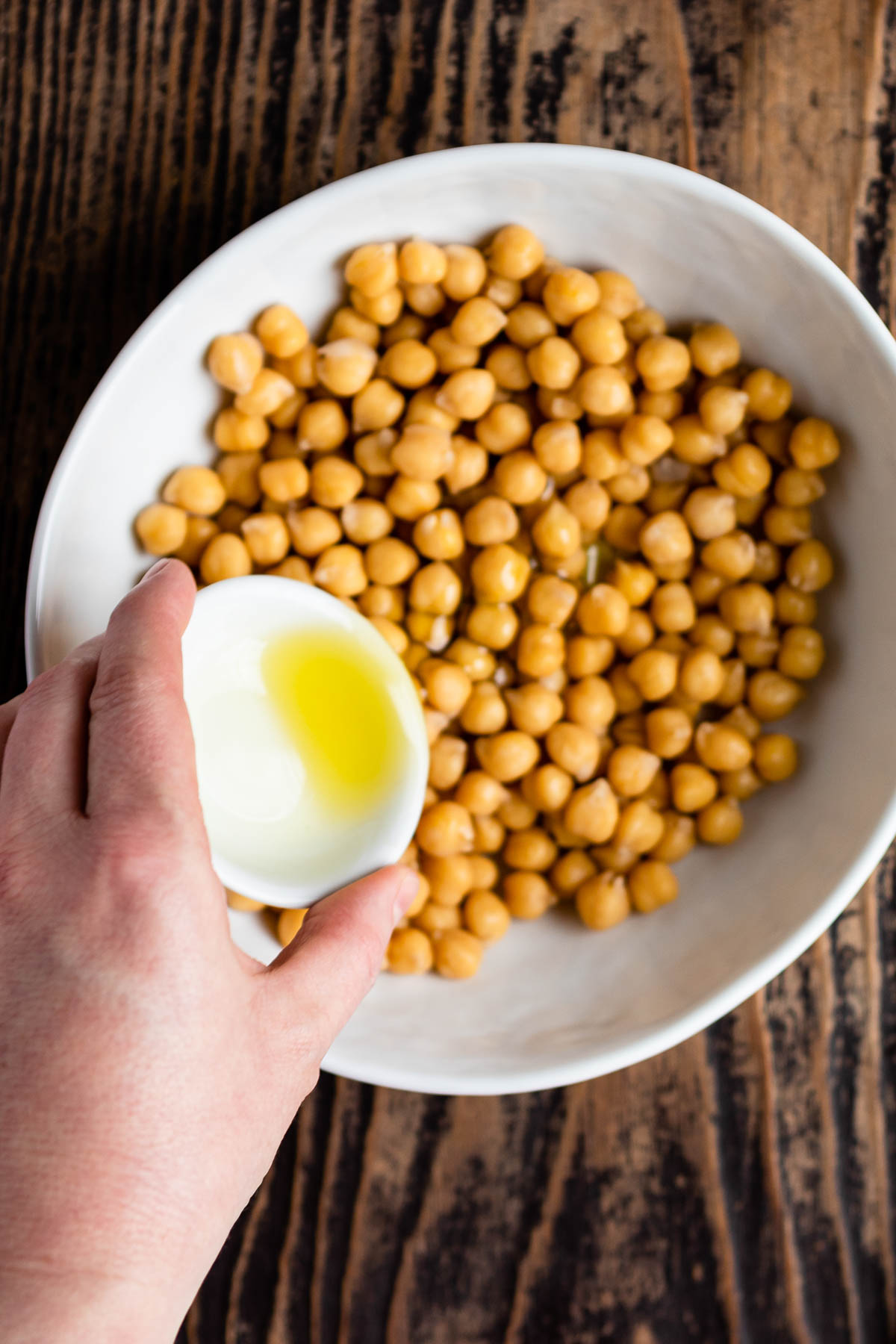 white bowl of garbanzo beans getting olive oil drizzled over them.