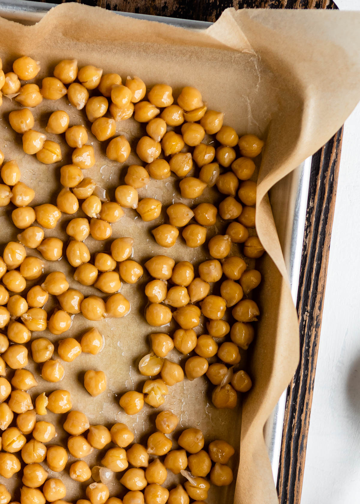 partially baked garbanzo beans on a parchment lined baking sheet, ready for more seasoning.