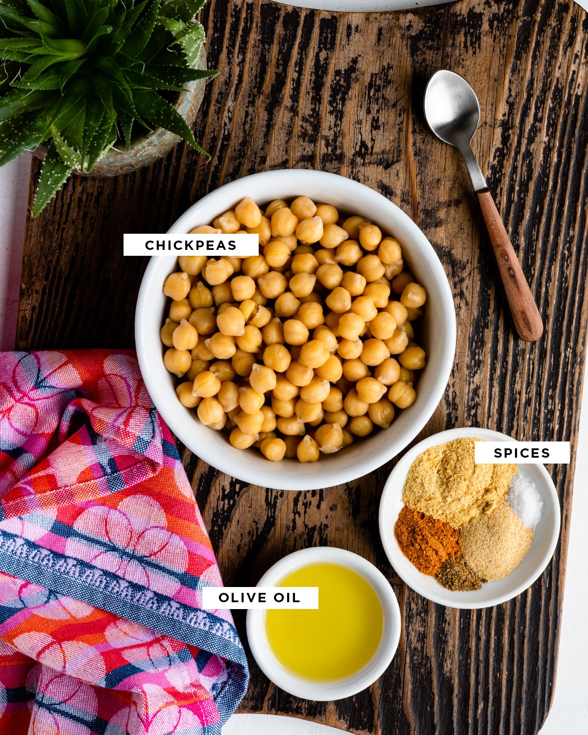 labeled ingredients for oven roasted chickpeas including chickpeas, spices and olive oil, all in individual white bowls.