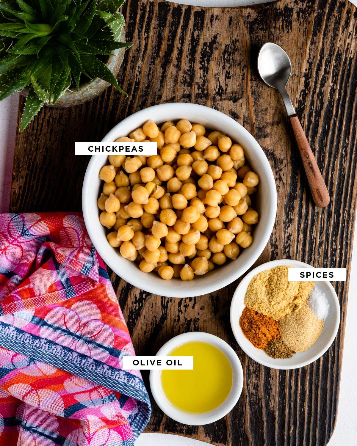 Labeled ingredients for oven-roasted chickpeas, including chickpeas, spices, and olive oil, all in individual white bowls.