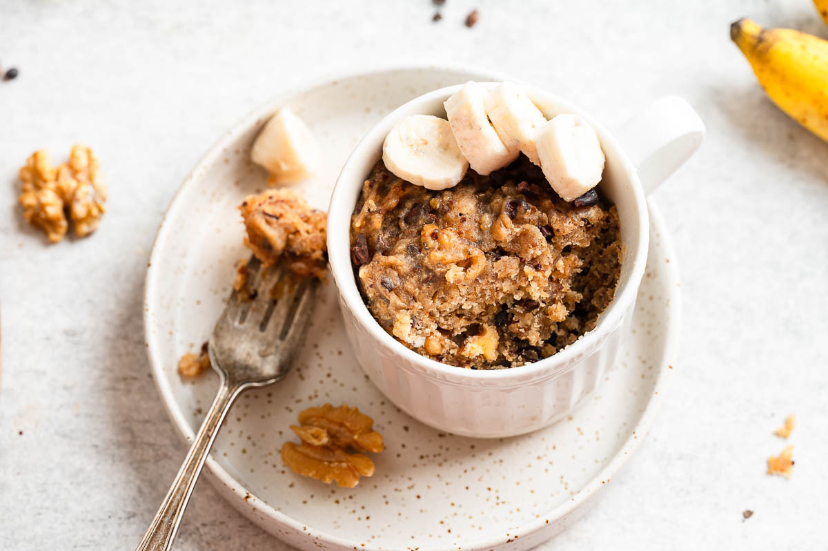 Banana bread mug cake topped with sliced banana and walnuts.