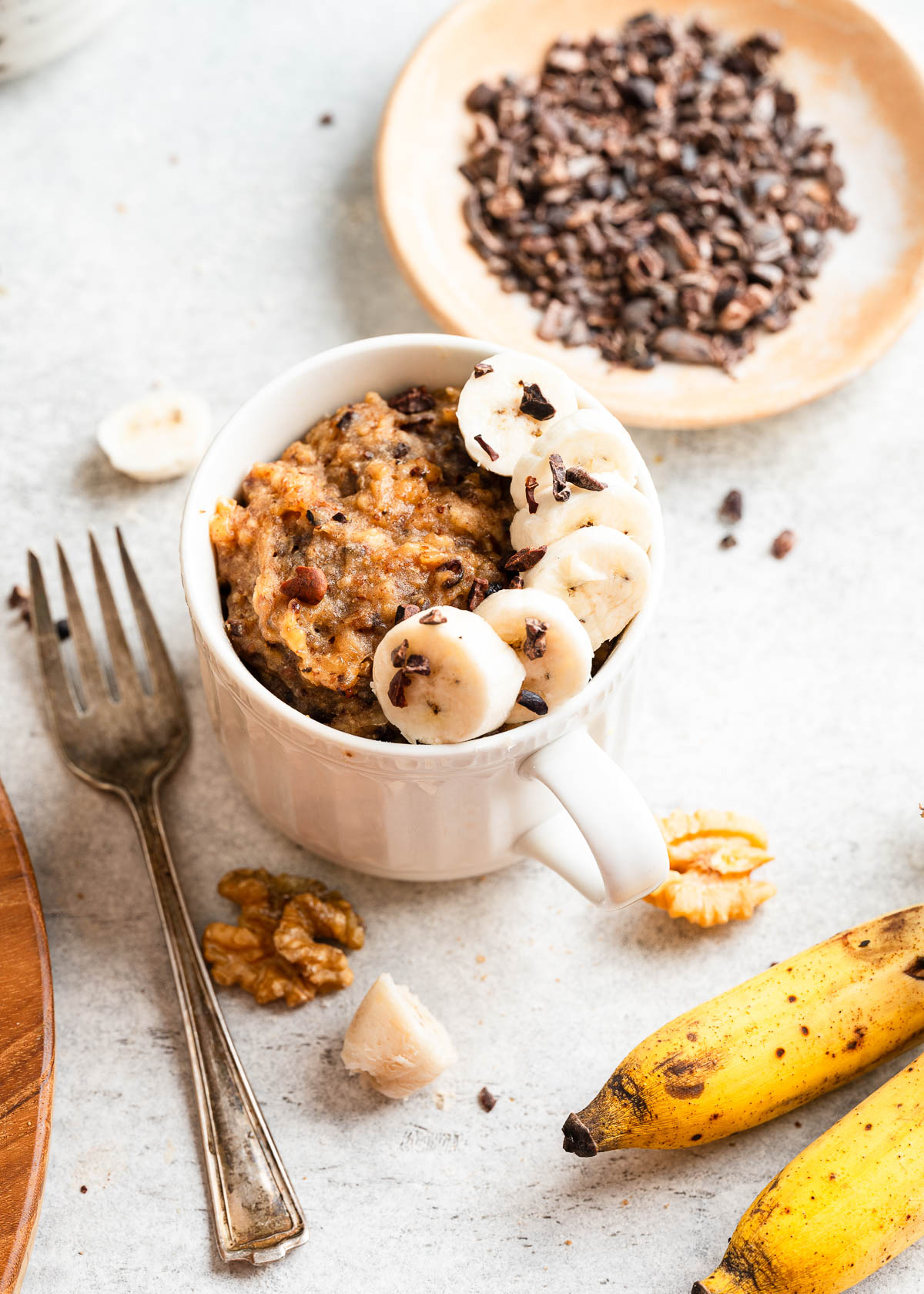 A single-serving banana mug cake in a white mug, garnished with banana slices.