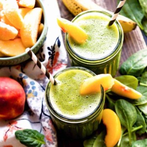 2 glass jars of banana peach smoothie with peach slices and paper straws.
