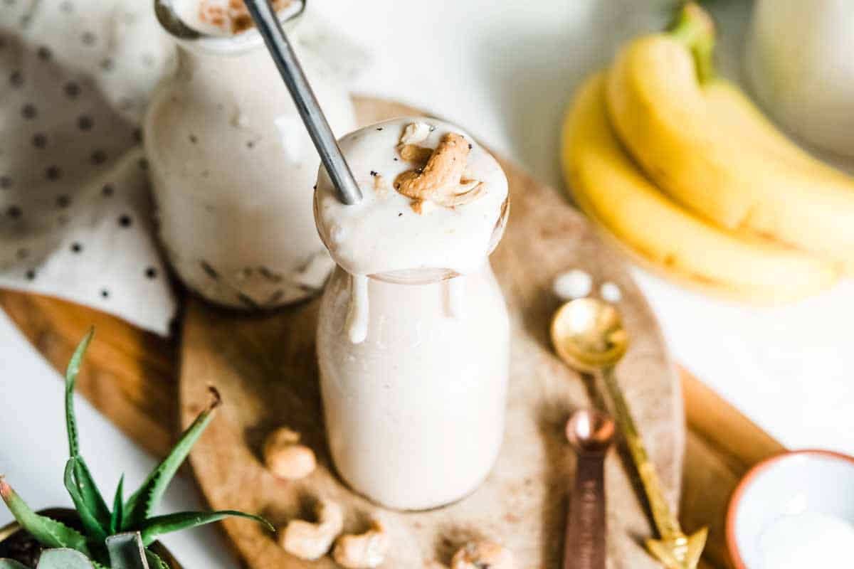 creamy white smoothie overflowing in a milkshake glass topped with cashews and a metal straw.