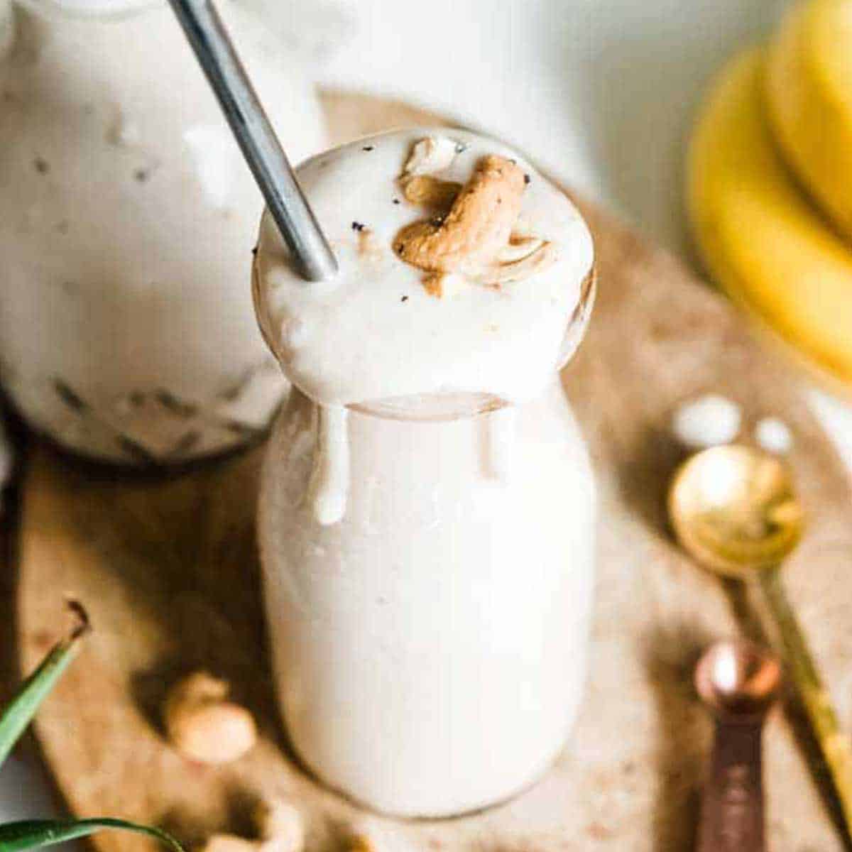banana smoothie in milkshake glass topped with cashews and metal straw.