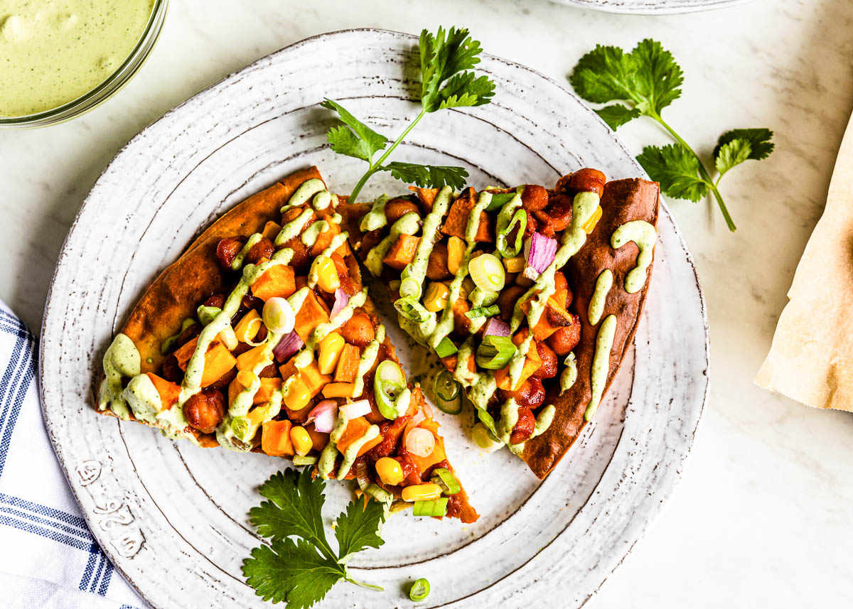 white plate with 2 slices of veggie pizza with green crema drizzled over top and sprigs of fresh cilantro garnish.