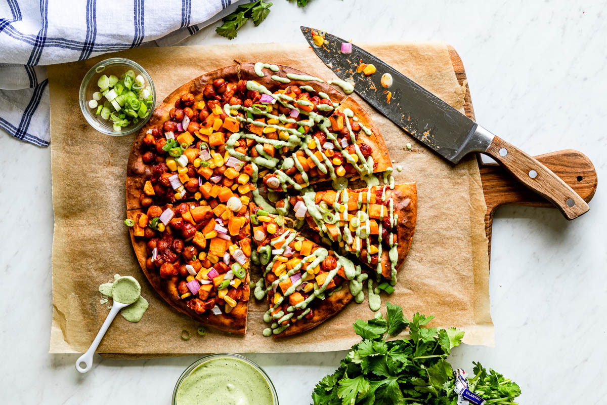 whole homemade pizza getting cut by a large knife on a parchment lined wooden platter.