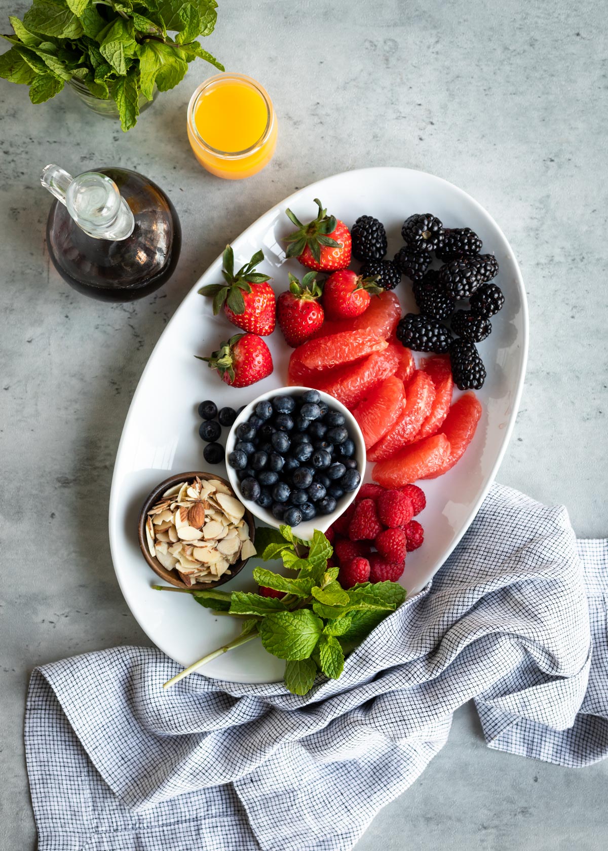 ingredients for berry fruit salad including blackberries, grapefruit, blueberries, raspberries, mint, and sliced almonds.