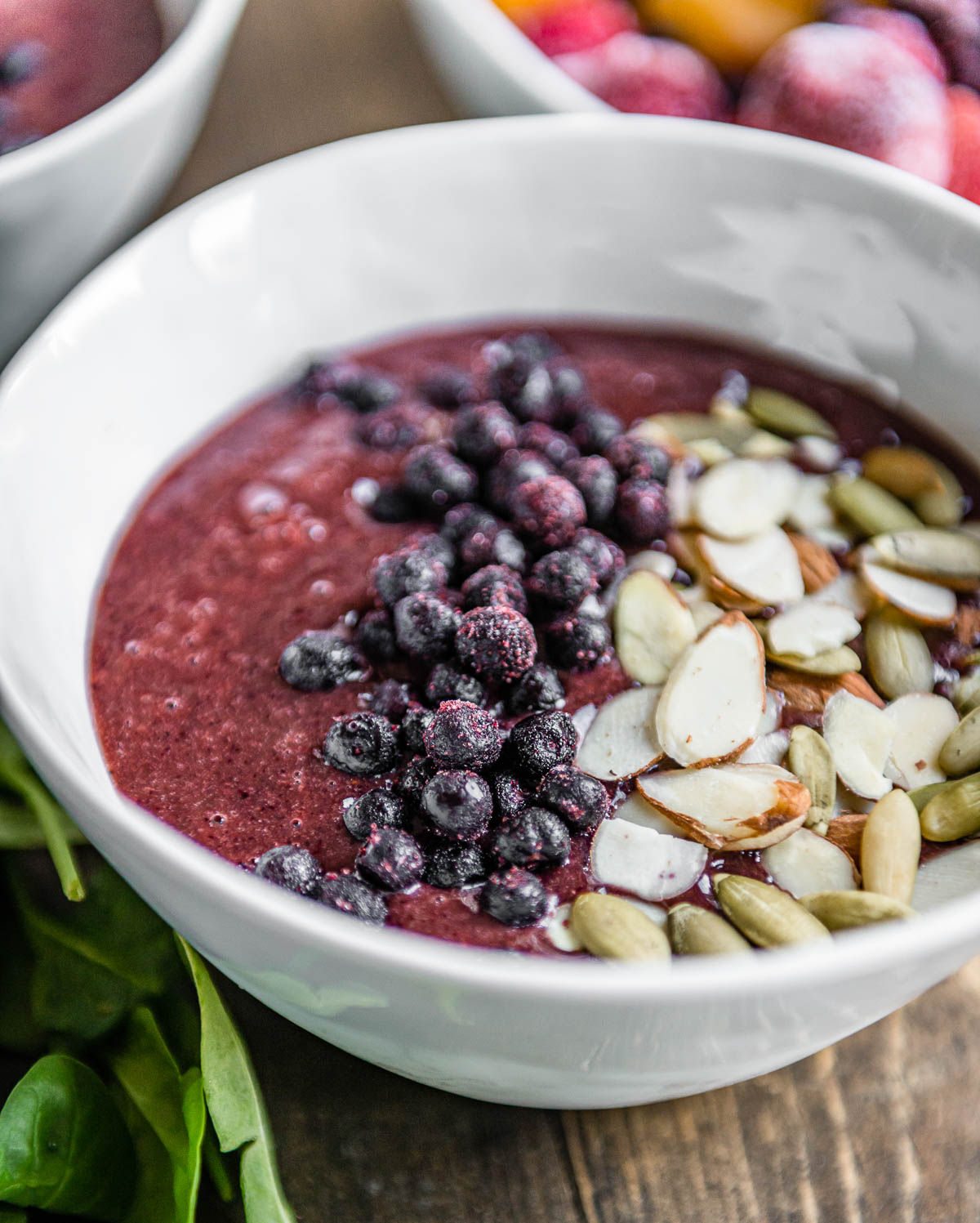 snack recipe in a white bowl topped with blueberries, sliced almonds and pepitas.