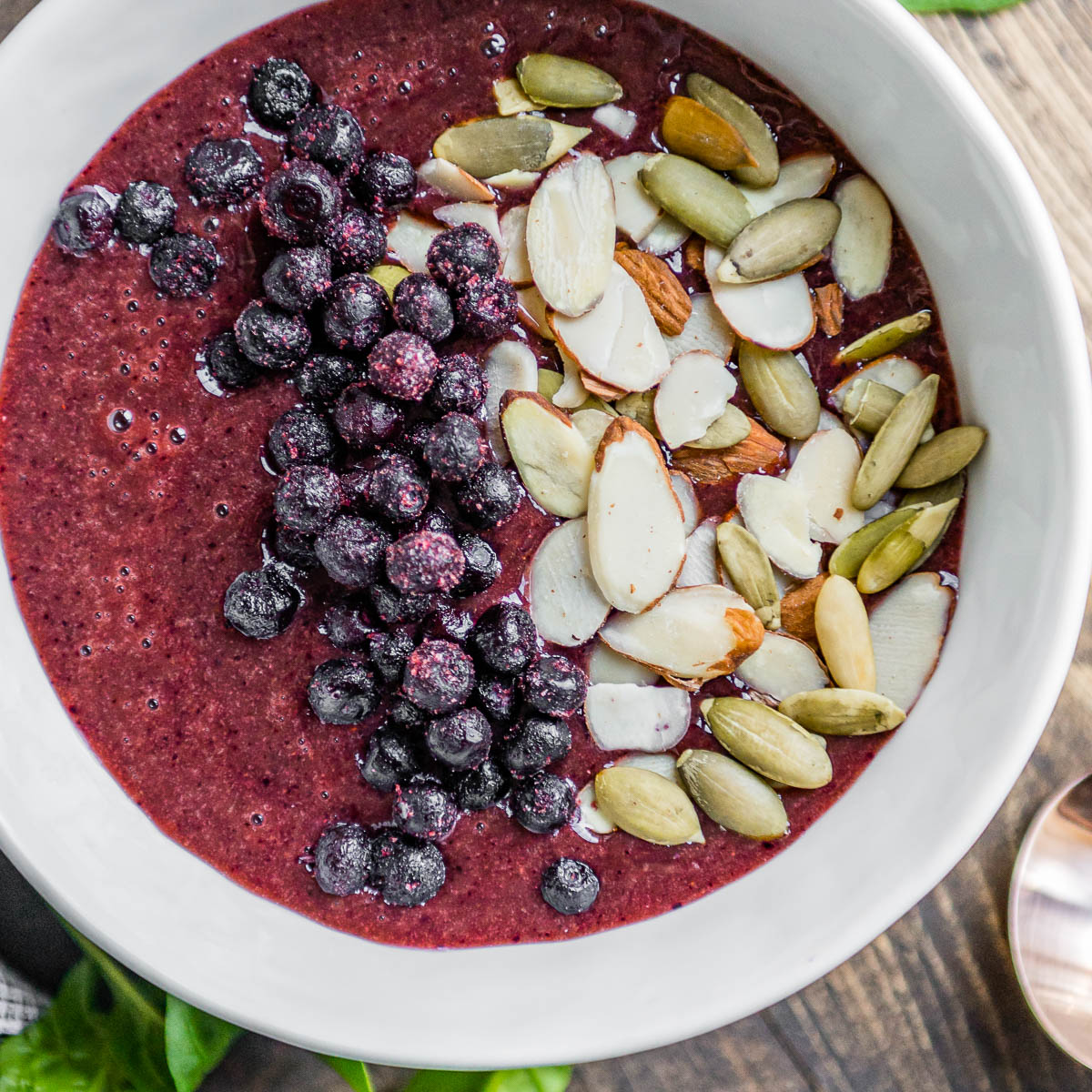 berry smoothie bowl in white bowl topped with frozen berries, sliced almonds and pepitas.