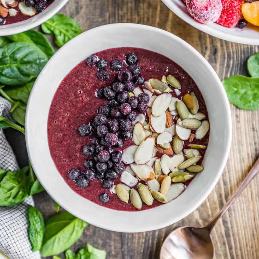 berry smoothie bowl in white bowl topped with frozen berries, sliced almonds and pepitas.