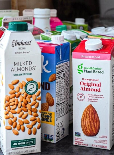 several cartons of different brands of store bought almond milk on a counter top.