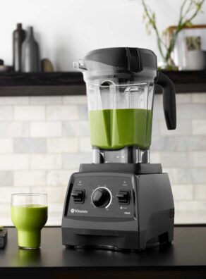 Vitamix pro blender on dark kitchen counter with green smoothie in a glass.