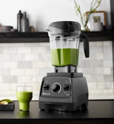 Vitamix pro blender on dark kitchen counter with green smoothie in a glass.
