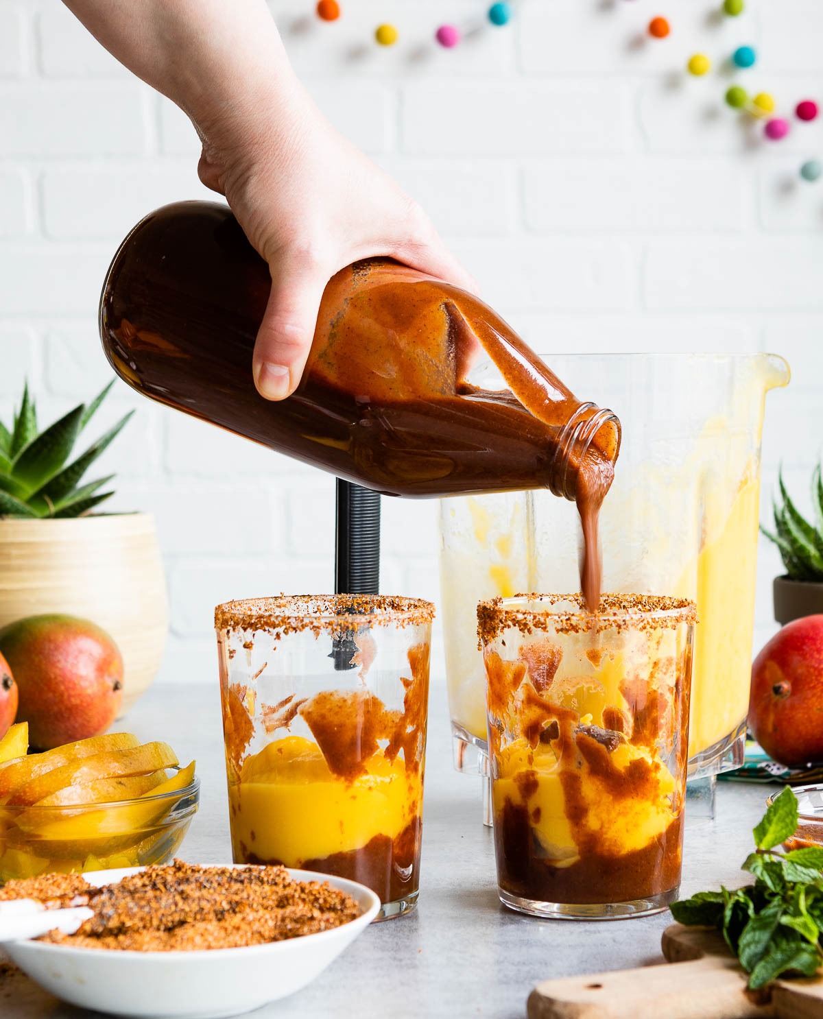 Pouring homemade chamoy sauce into glasses with mangonada.
