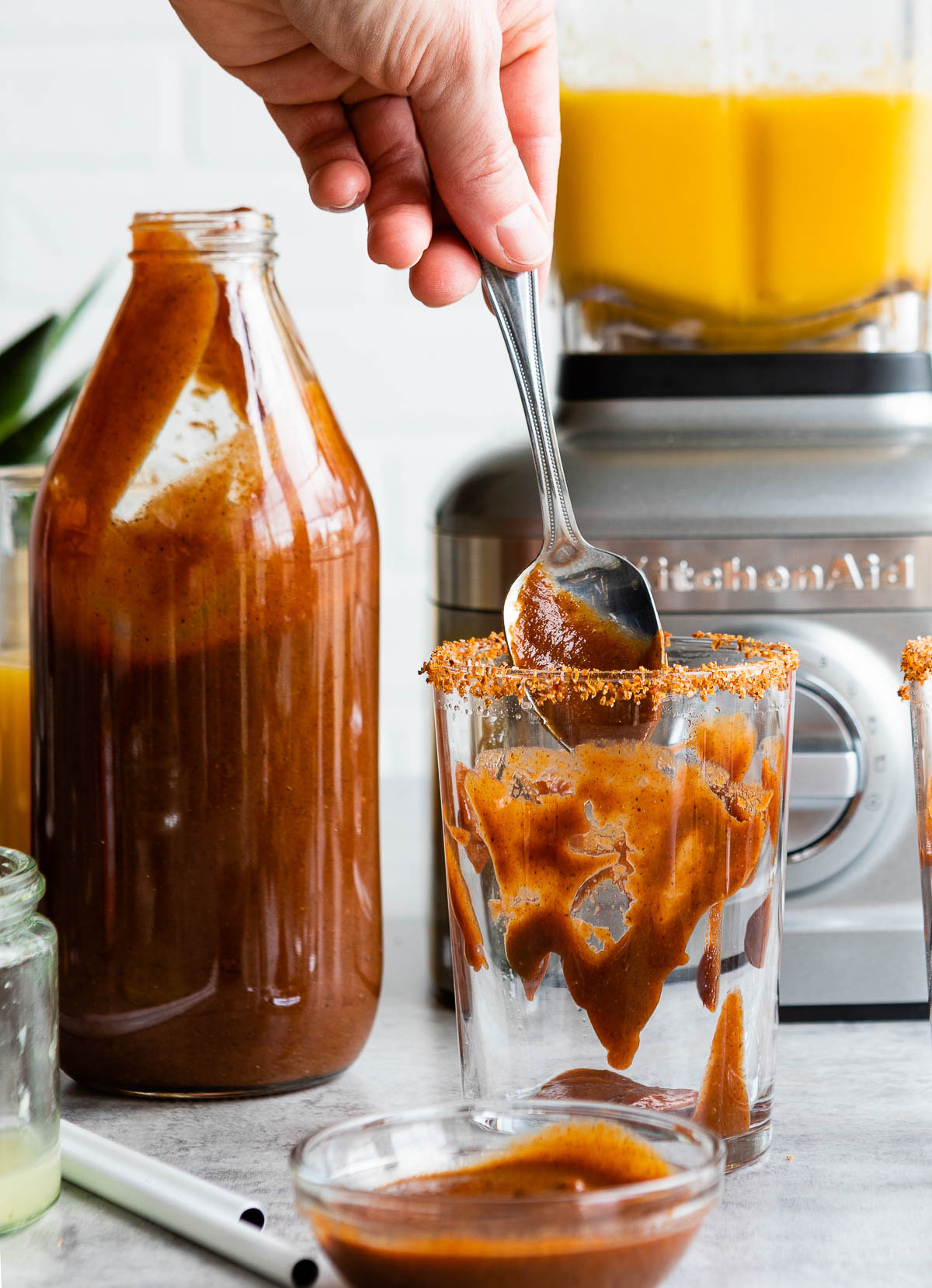 Spoon with the best chamoy sauce recipe in a glass with tajin on rim.