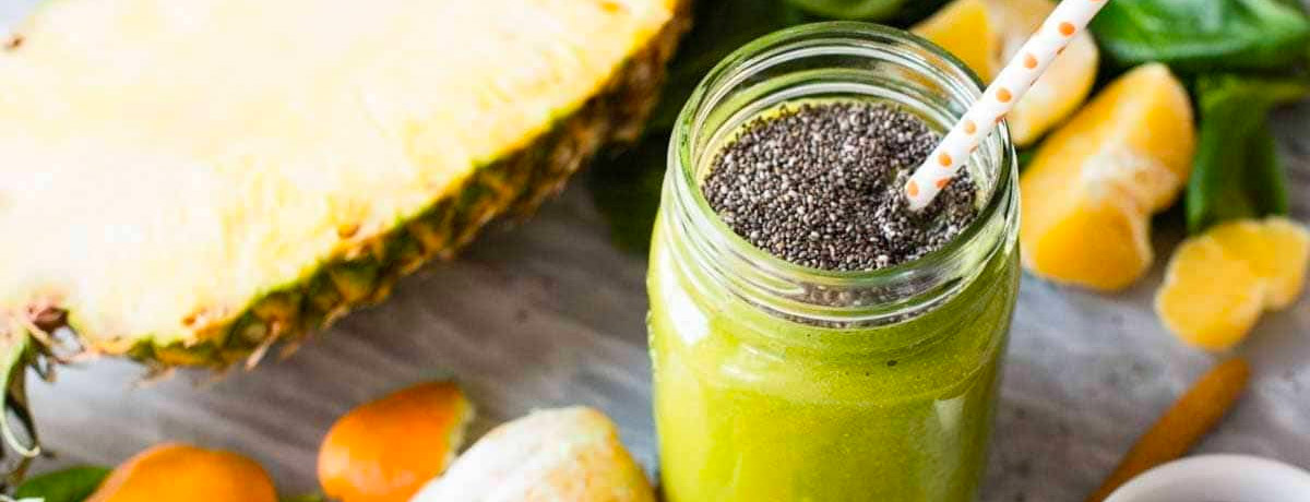 green smoothie in a jar with chia seeds sprinkled on top and a halved pineapple in the background