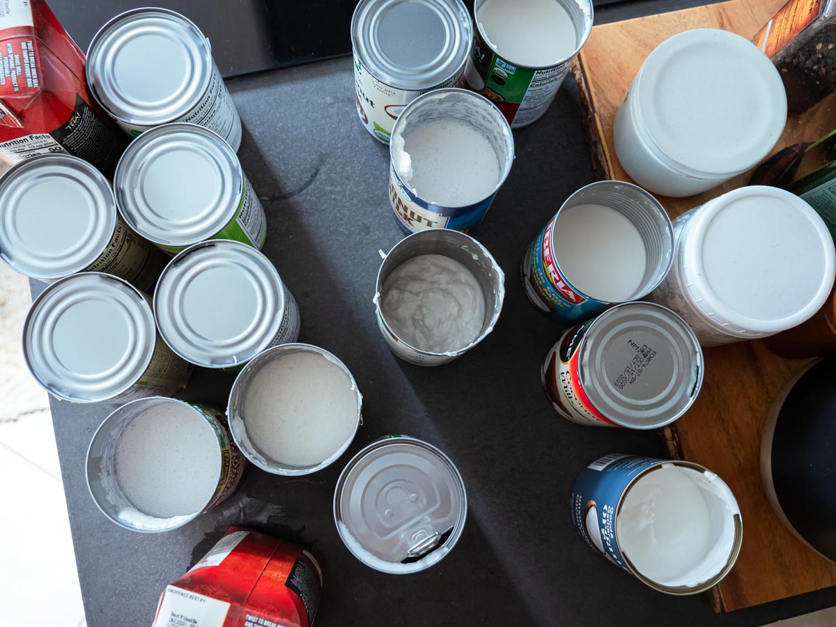 several opened cans of dairy-free milk ready to be taste-tested on a kitchen counter.