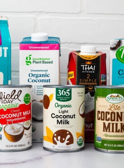 7 coconut milk brands grouped on a countertop with a white brick background.