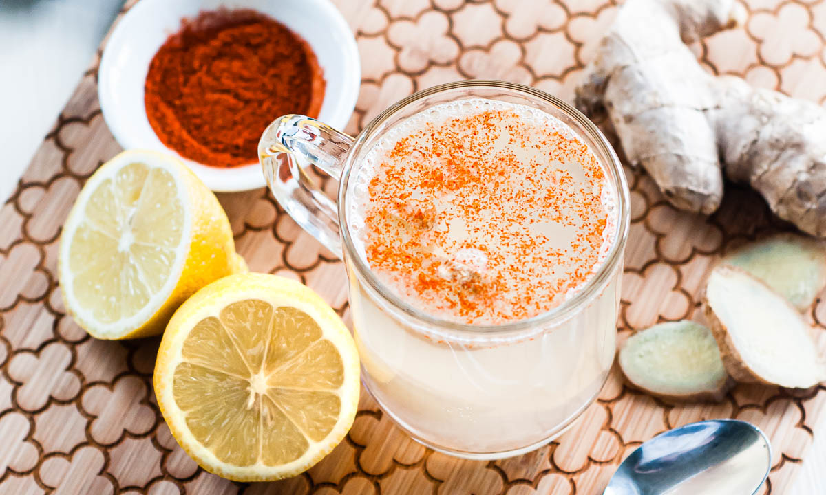 Glass mug of the best detox tea recipe, topped with cayenne pepper and ginger root, on a wooden cutting board surrounded by lemon and ginger, makes for an effective homemade weight loss tea.