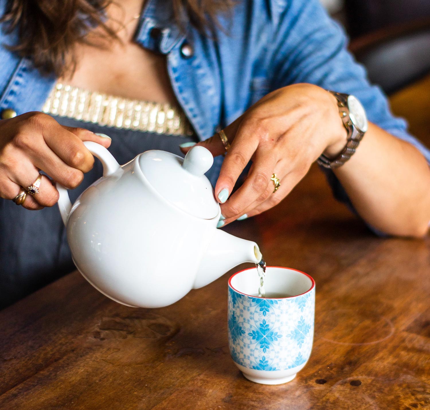 woman in blue shirt pouring warm water into tea cup.