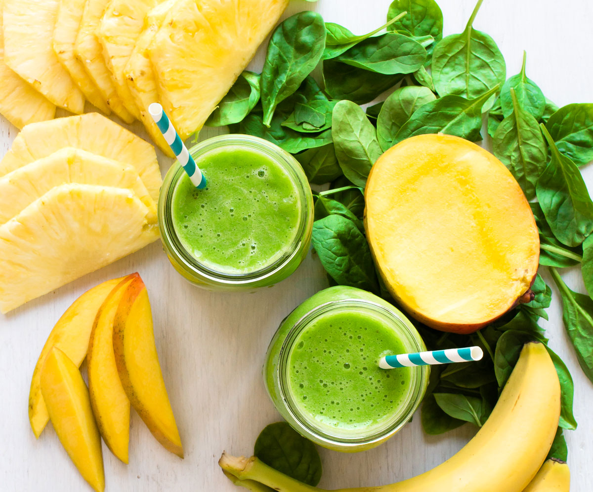 Overhead view of green smoothies in glass jars with straws.