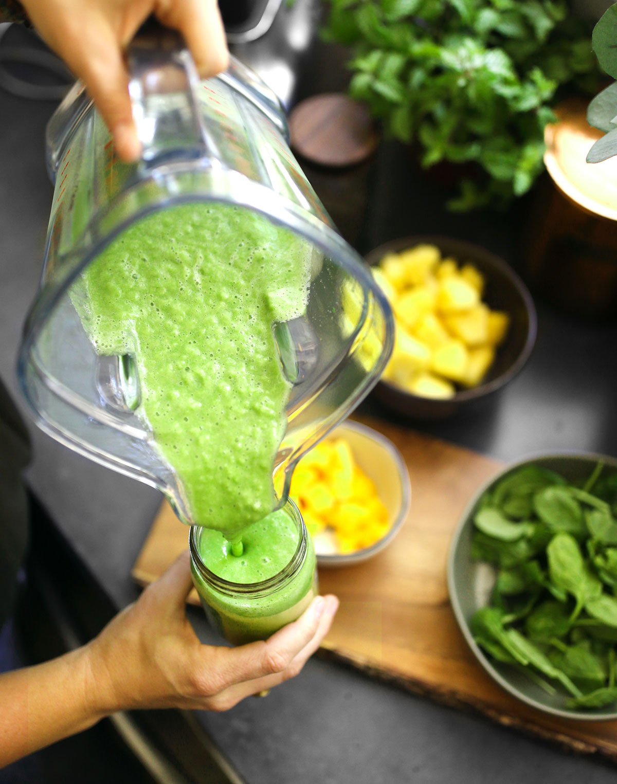 Pouring a green smoothie from a blender into a glass cup.