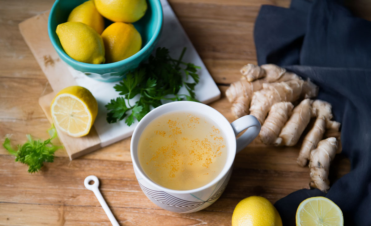 Detox tea in a glass mug surrounded by cayenne pepper, ginger root, and a whole lemon is a great example of a homemade detox tea recipe.