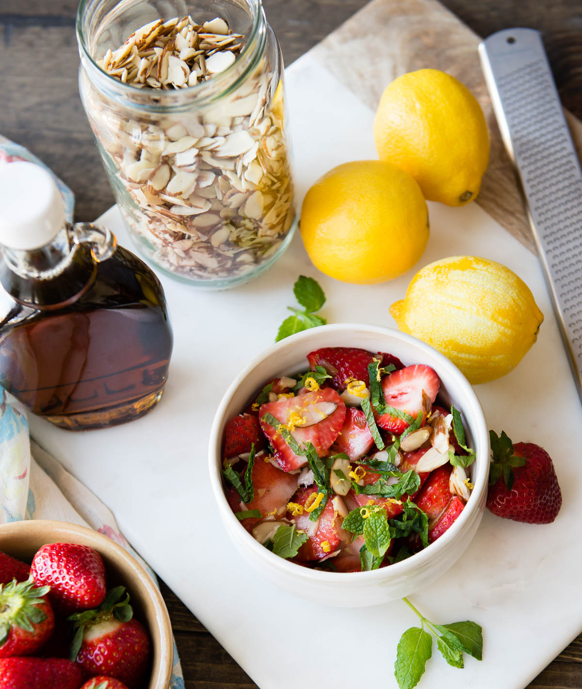 bowl of sliced strawberries topped with lemon zest, mint and sliced almonds.