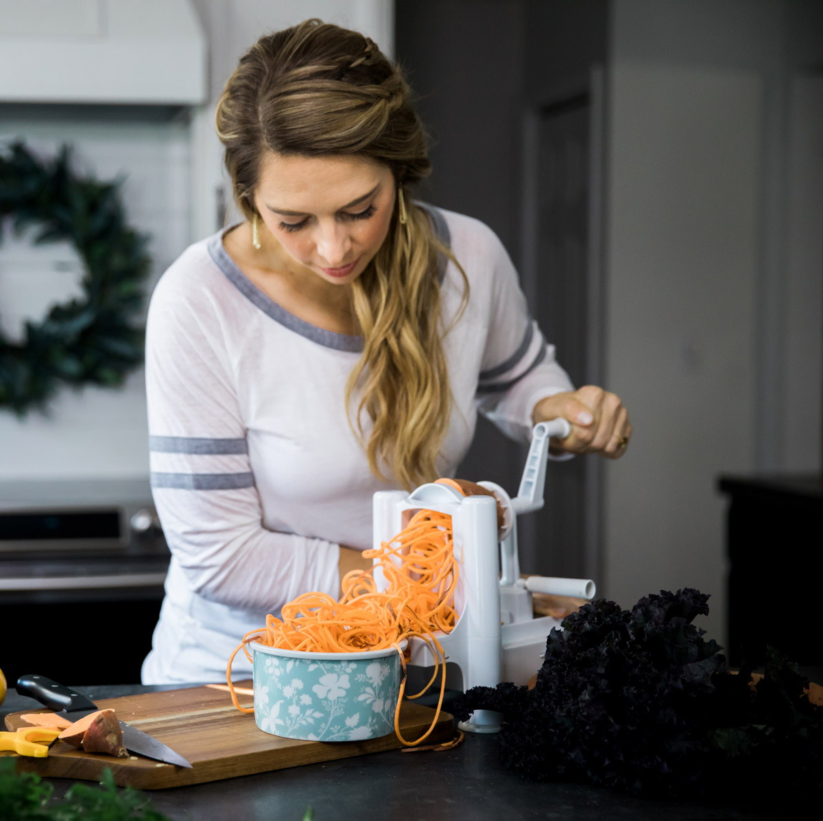 Young woman spiralizing a sweet potato in a white kitchen with gray concrete countertop.