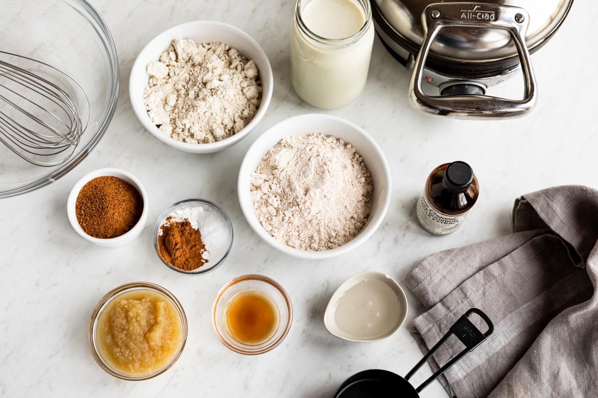 ingredients for vegan waffle recipe including oat milk, vanilla, whole wheat flour, oat flour, vinegar, cinnamon and unsweetened applesauce.