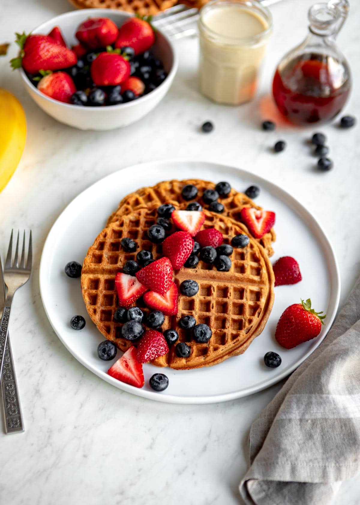breakfast waffles topped with blueberries and strawberries on a white plate.