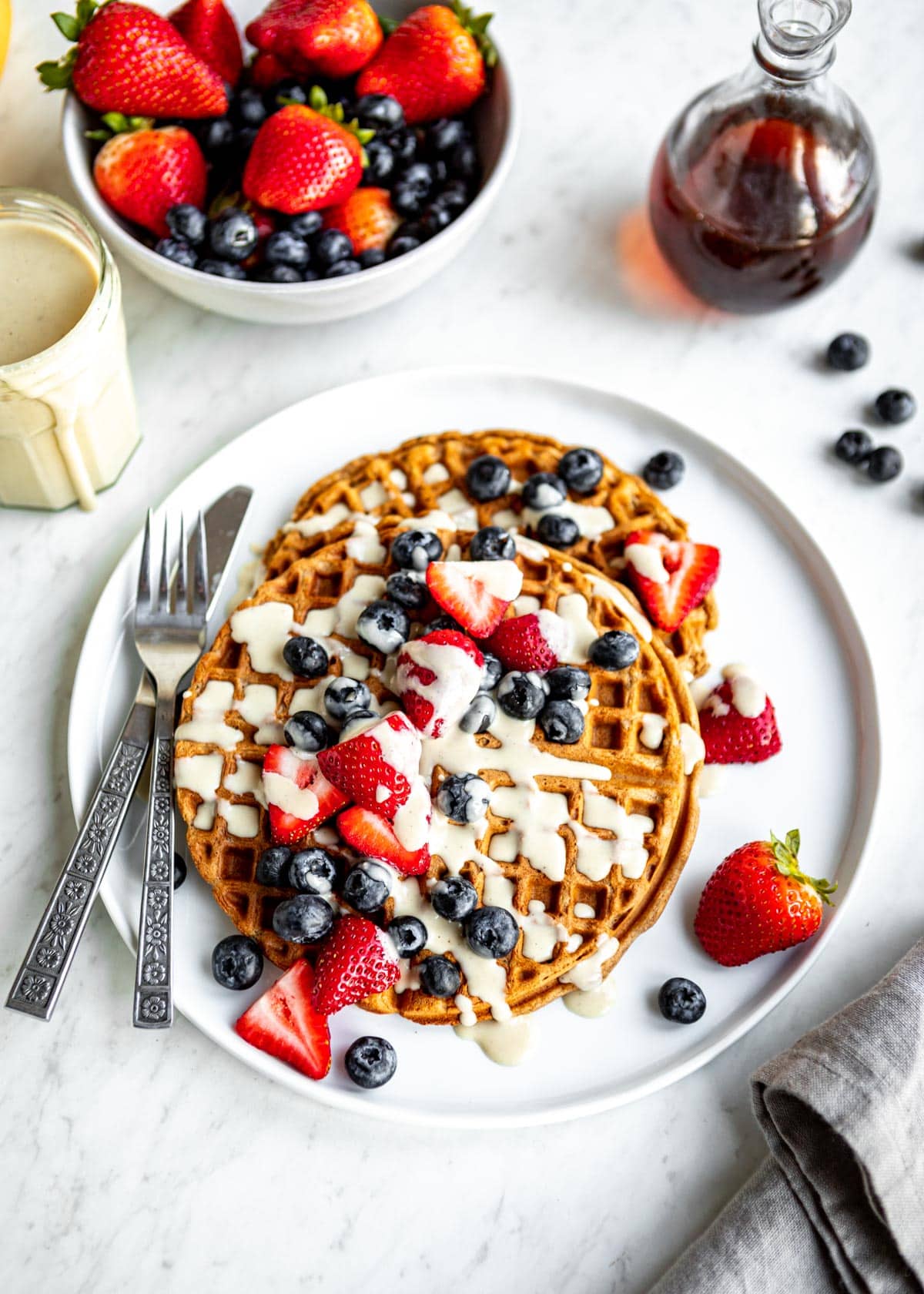 best vegan waffles on a white plate with fresh berries, a knife and a fork.