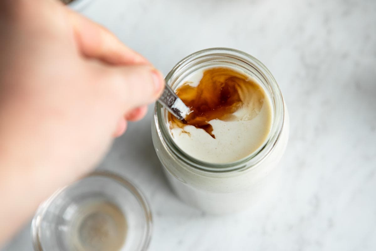 maple cashew cream in a jar, getting stirred with a stainless steel spoon.
