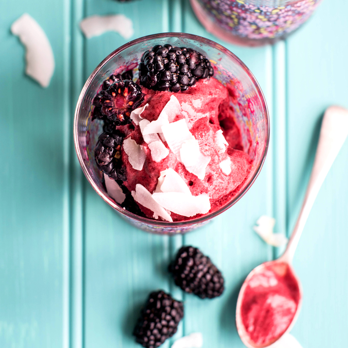 Blackberry coconut sorbet in clear glass on teal countertop with fresh fruit.