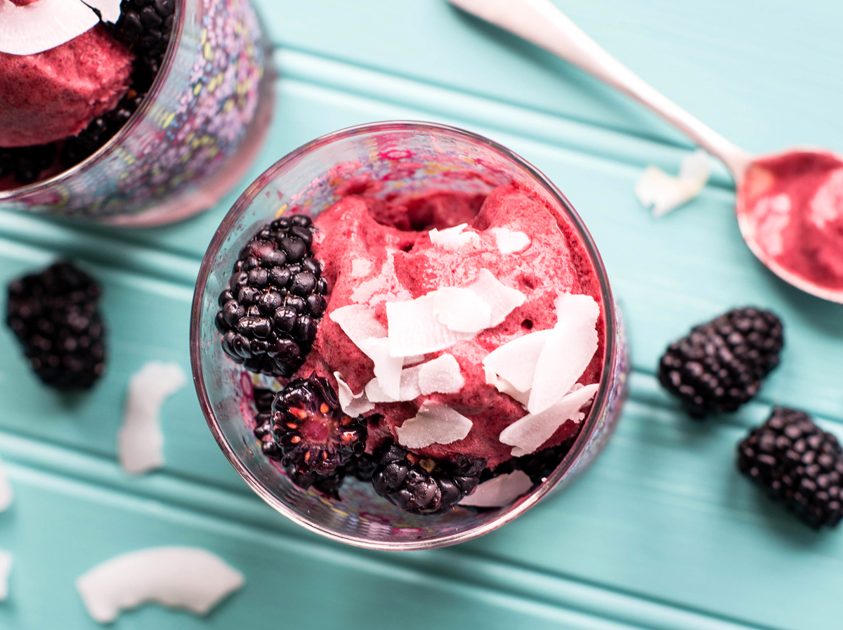 A pair of blackberry coconut sorbet treats in glass cups on a blue countertop.