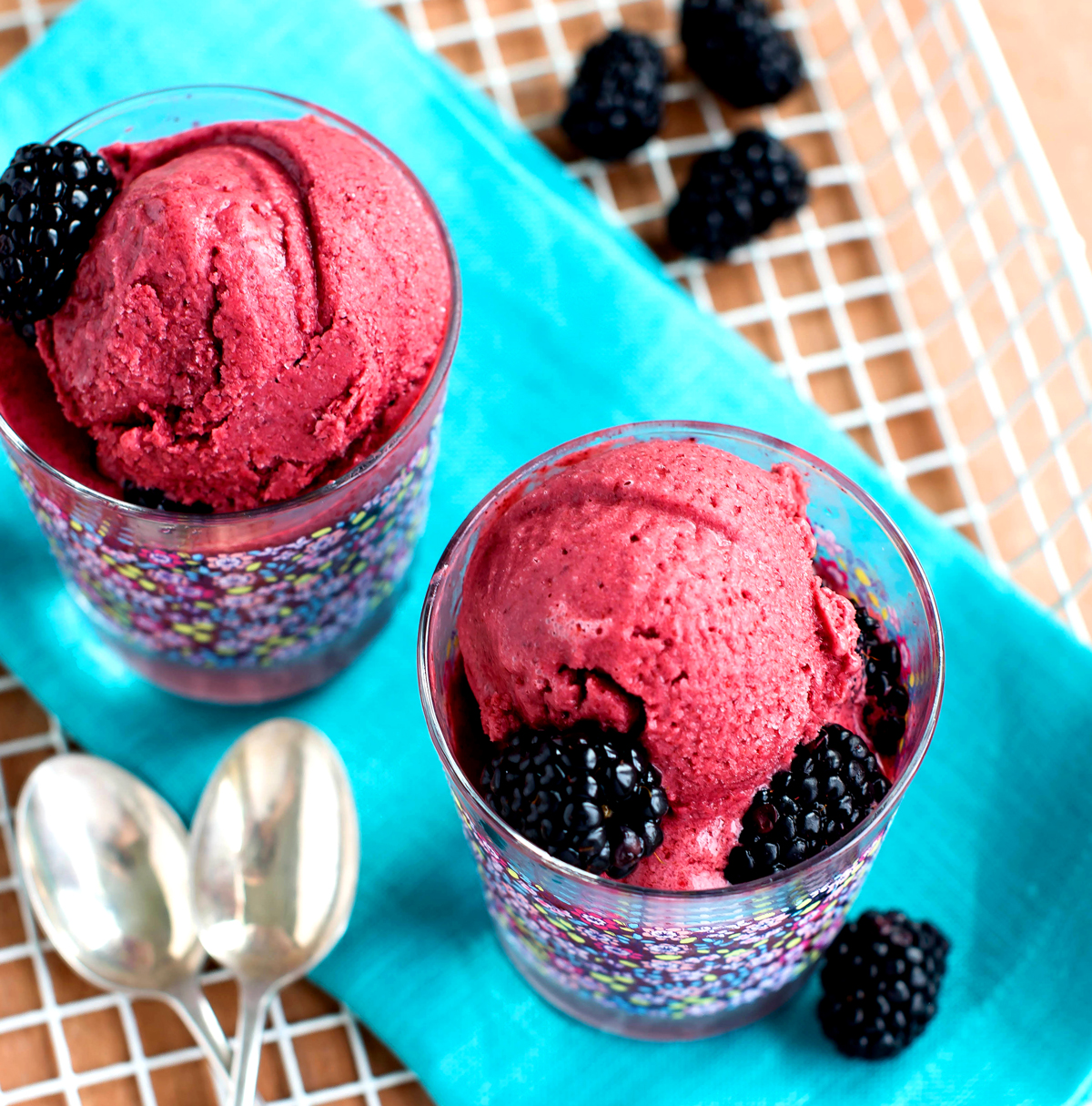 White basket with teal linen napkins alongside glass cups with red sorbet and fresh blackberries piled on top.