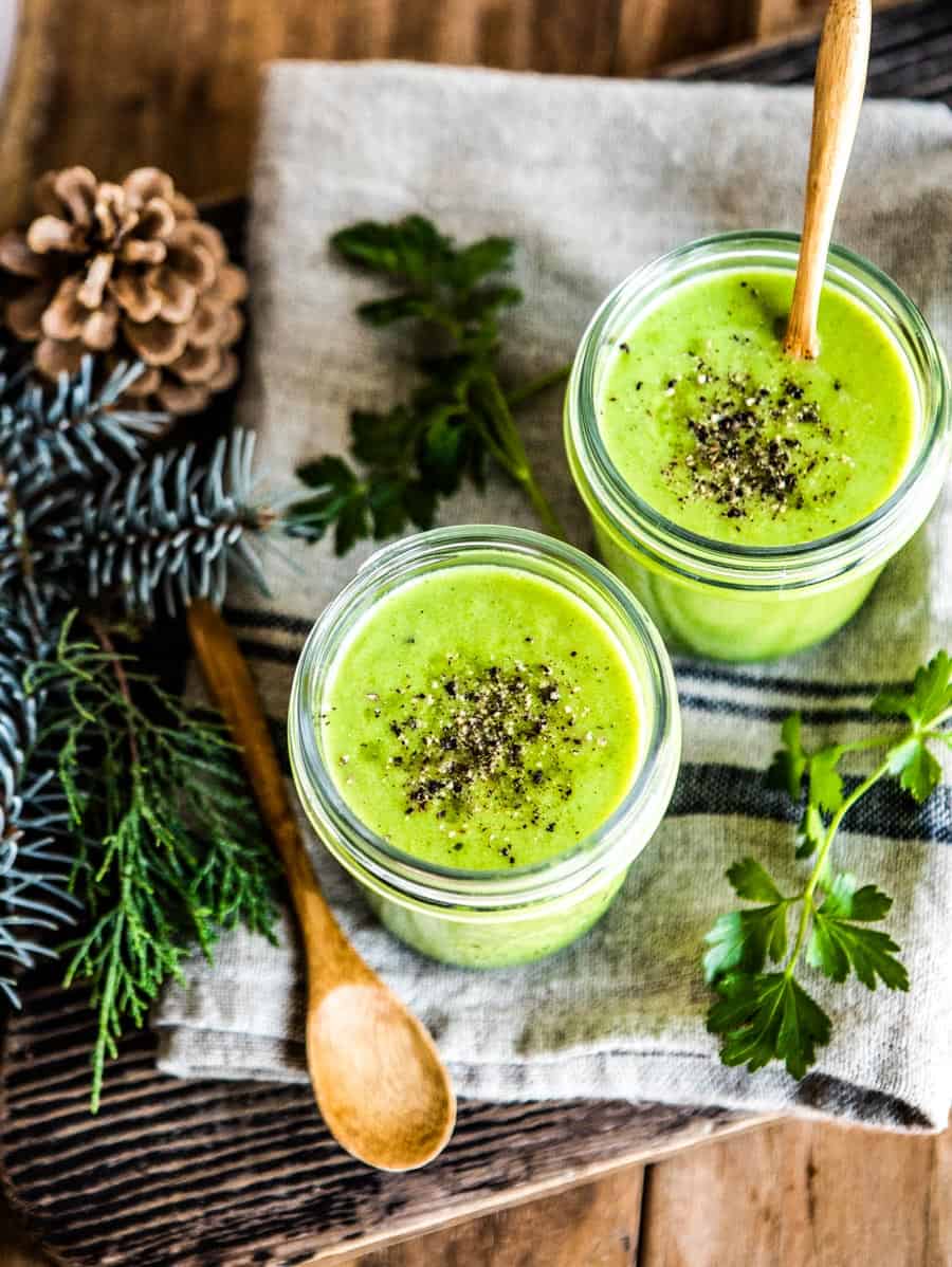 delicious blended vegetable soup in 2 glasses topped with black pepper and a wooden spoon.