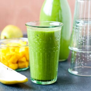 a tall glass of brain food smoothie along side sliced pears and mango.