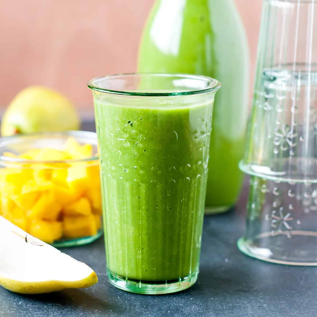 a tall glass of brain food smoothie along side sliced pears and mango.
