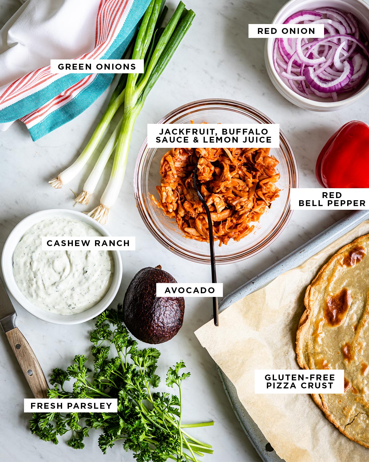 labeled ingredients including red onion, green onions, jackfruit mixed with buffalo sauce and lemon juice, red bell pepper, cashew ranch, avocado, fresh parsley and gluten-free pizza crust.