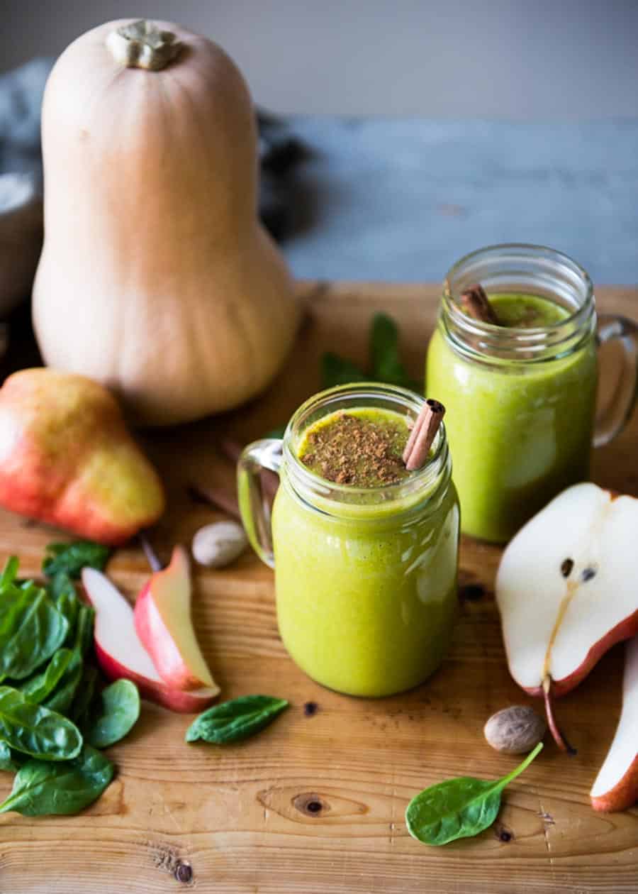 green smoothie in a glass mug with a cinnamon stick sticking out of the top.