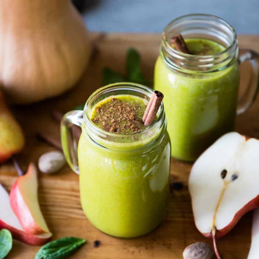 2 glasses of butternut squash smoothie with cinnamon sticks on top next to half a pear.